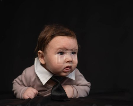 Porträt eines auf dem Bauch liegenden Babys mit Krawatte auf schwarzem Hintergrund
