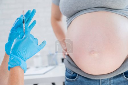 El médico le administra una inyección en el estómago de una mujer embarazada
