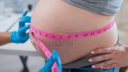 Téléchargez les photos : Médecin mesurant le volume de l'abdomen d'une femme enceinte à l'aide d'une bande en pouces - en image libre de droit