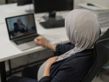 Eine schwangere Frau im Hidschab kommuniziert mit einem Kollegen per Videokonferenz auf einem Laptop