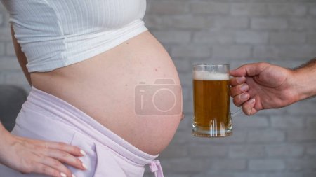 A man clinks a bottle of beer with a pregnant womans belly