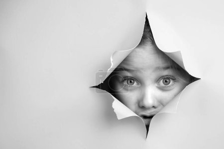 Cute Caucasian girl peeks out of a hole in a paper background