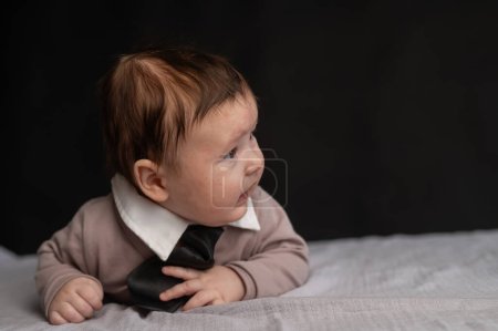 Porträt eines auf dem Bauch liegenden Babys mit Krawatte auf schwarzem Hintergrund