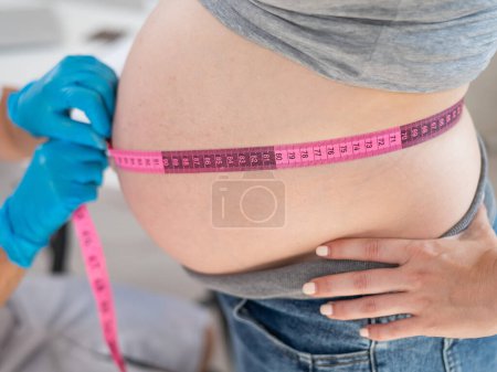 Téléchargez les photos : Médecin mesurant le volume de l'abdomen d'une femme enceinte à l'aide d'une bande centimétrique - en image libre de droit