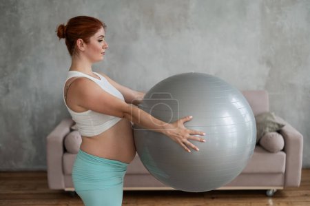 Schwangere rothaarige Frau macht zu Hause Armübungen mit Fitball