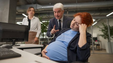 Elderly Caucasian man and woman giggling behind their sleeping pregnant colleague in the office
