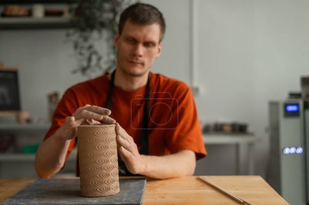 Potter sculpts a patterned cylinder from clay