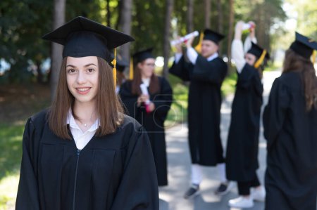 Téléchargez les photos : Group of happy students in graduation gowns outdoors. A young girl is happy to receive her diploma - en image libre de droit