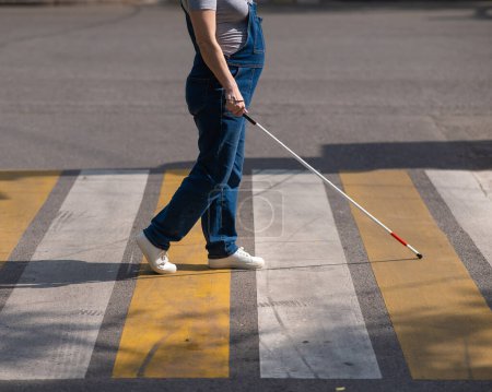 Photo for Close-up of the legs of a blind woman crossing the road at a crosswalk with a cane - Royalty Free Image