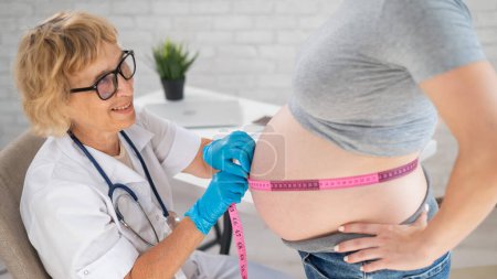 Téléchargez les photos : Médecin mesurant le volume de l'abdomen d'une femme enceinte à l'aide d'une bande centimétrique - en image libre de droit