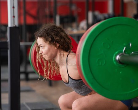 Photo for Middle-aged woman doing squats with a barbell in the gym - Royalty Free Image
