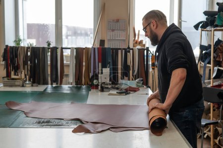 Leatherworker unrolls rolls of leather in workshop