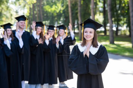 Téléchargez les photos : Groupe d'étudiants heureux en robes de remise des diplômes à l'extérieur. Une jeune fille au premier plan - en image libre de droit