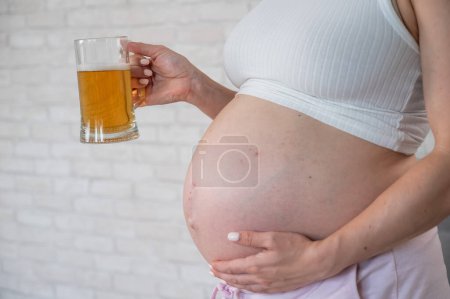 Faceless pregnant woman with rash on stomach holding glass of beer