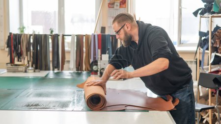 Leatherworker unrolls rolls of leather in workshop