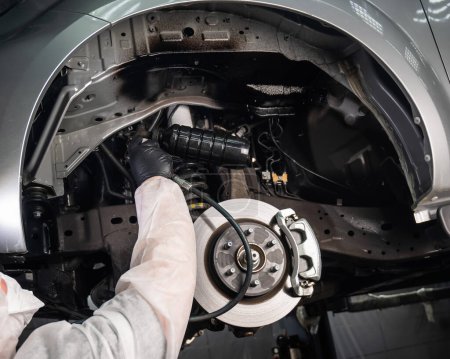 Un mecánico automático aplica masilla anticorrosión a la parte inferior de un coche