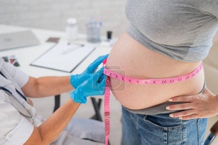 Téléchargez les photos : Médecin mesurant le volume de l'abdomen d'une femme enceinte à l'aide d'une bande en pouces - en image libre de droit