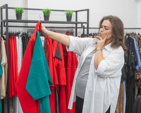 Una mujer gorda elige ropa en una tienda de tallas grandes