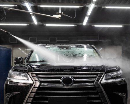 Foto de Un hombre lava espuma de un coche negro con agua en un lavado de coches - Imagen libre de derechos