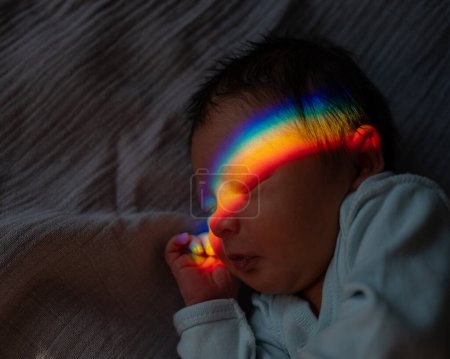 Nahaufnahme eines neugeborenen Jungen mit einem Prismenstrahl im Gesicht. Regenbogen