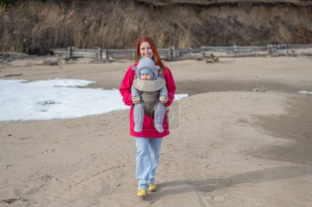 Caucasian red-haired woman walks with her son in an ergo backpack in nature in winter