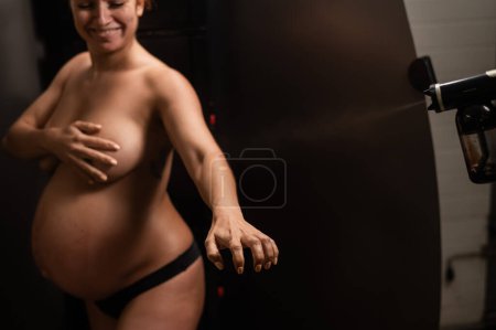Foto de El maestro aplica bronceador con un aerosol en las manos de una mujer embarazada. Bronceado instantáneo - Imagen libre de derechos
