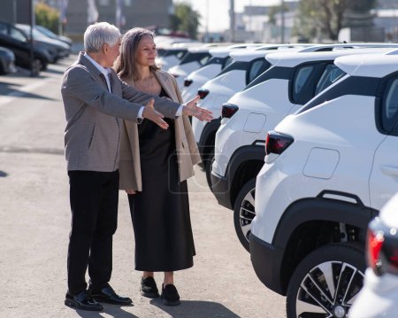 Mature couple caucasien passe devant les voitures à l'extérieur, en choisissant un nouveau