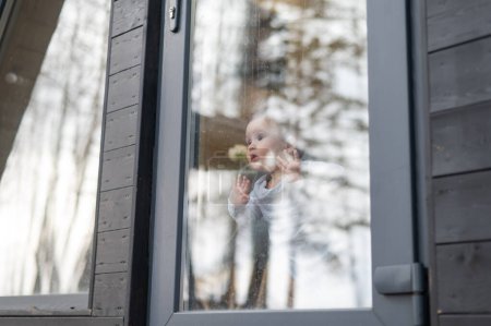 Bébé garçon debout près de la fenêtre patio