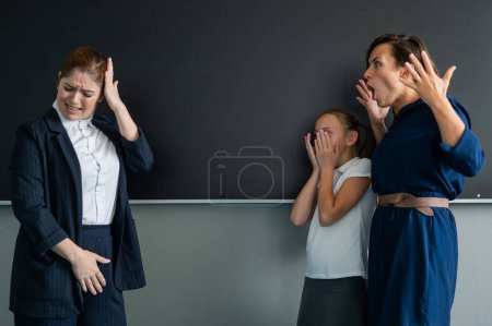Schoolgirl and her mother yell at the teacher standing at the blackboard