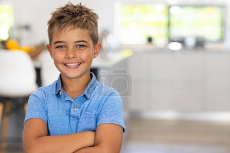 Portrait of caucasian cute boy with arms crossed smiling while standing at home, copy space. Unaltered, lifestyle, childhood, happy and home concept.