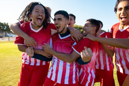 Multiracial male team players screaming while celebrating victory after soccer match at playground. Unaltered, soccer, sport, teamwork, togetherness, competition, winning, happy and achievement.
