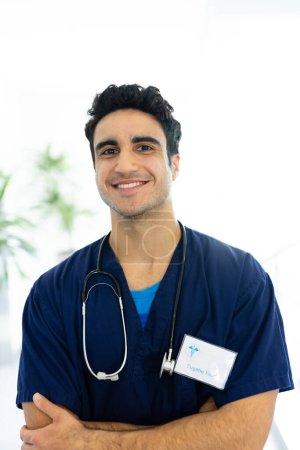 Vertical portrait of smiling biracial male doctor in hospital corridor, with copy space. Hospital, medical and healthcare services.