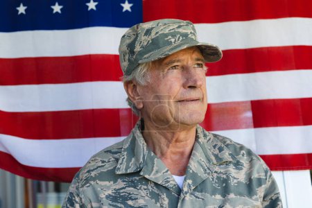 Close-up of caucasian army soldier wearing camouflage clothing looking away against flag of america. Cap, confidence, copy space, unaltered, senior, pride, military, armed forces and patriotism.