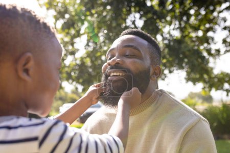 African american cheerful son holding father's beard while playing in backyard during weekend. Unaltered, lifestyle, family, love, togetherness, childhood and enjoyment concept.