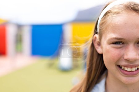 Halbgesichtiges Porträt einer lächelnden kaukasischen Schülerin auf dem Schulhof, mit Kopierraum. Bildung, Inklusion, Grundschule und Lernkonzept.