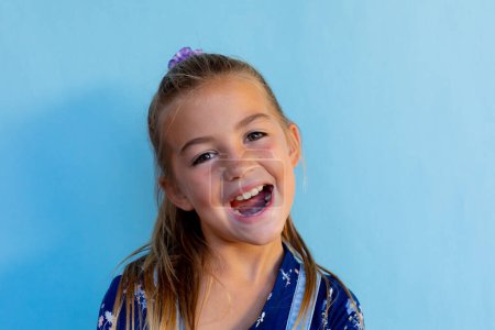 Portrait of happy caucasian schoolgirl with ponytail over blue background at elementary school. Education, childhood, development, learning and school, unaltered.
