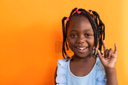 African american schoolgirl doing sign language gestures over orange background at elementary school. Disability, education, childhood, development, learning and school, unaltered.