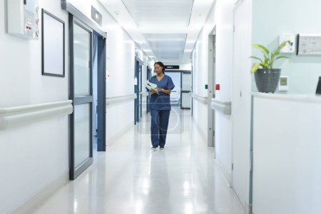 African american female doctor with documents walking in hospital corridor. Medicine, healthcare and medical services, unaltered.