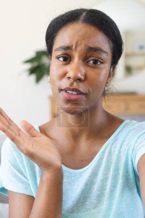 Mujer birracial joven se ve confundida en un entorno de casa en una videollamada. Su expresión sugiere que está lidiando con una situación o pregunta desconcertante..