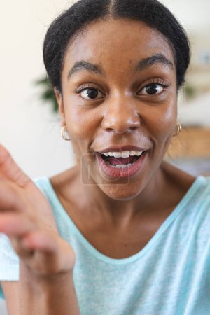 Excited young biracial woman gestures animatedly at home on video call. Her lively expression adds a personal touch to the cozy indoor setting.
