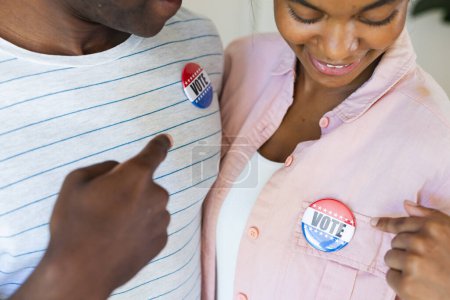 Biracial woman and African American man show their 'Vote' badges. They promote civic engagement and the importance of voting in a democratic society.