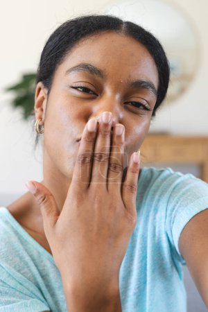 Young biracial woman sends a kiss at home on a video call. She's expressing affection or saying goodbye in a casual indoor setting.