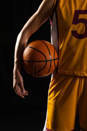 Jugador de baloncesto en acción sobre un fondo oscuro con un fondo negro. El enfoque y la determinación del atleta son evidentes en la postura equilibrada y el agarre en la pelota.