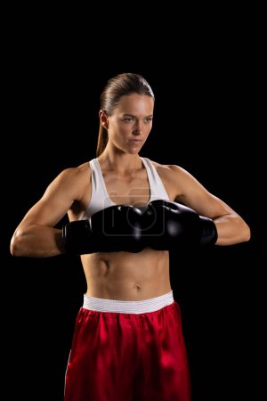 Young Caucasian woman poses confidently in boxing gear, with copy space. Her athletic form and focused expression convey strength and determination.
