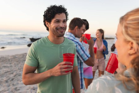 Diverse group of friends enjoy a beach party at sunset. They share laughs and drinks in a casual outdoor gathering.