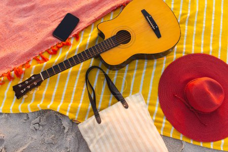 Eine Gitarre, ein Hut und ein Smartphone ruhen auf einer Stranddecke mit Kopierraum. Das Wesentliche am Strand fängt die Essenz eines erholsamen Tages am Meer ein.