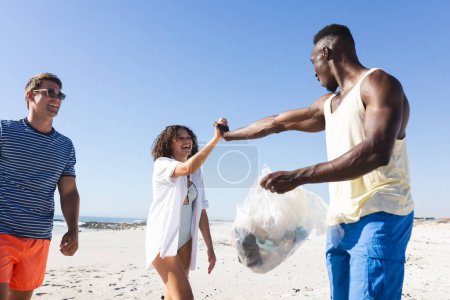 Diverse friends clean up a beach together, collecting trash. They show teamwork in an outdoor environmental conservation effort.