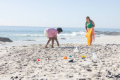 Young Caucasian woman and African American man clean a beach by collecting trash with copy space. They demonstrate environmental responsibility by picking up litter outdoors. tote bag #702385970