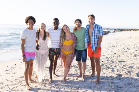 Diverse group of friends enjoy a sunny day at the beach. Their smiles suggest a relaxing and fun outdoor gathering.