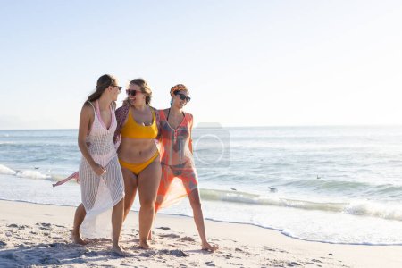 Three young women enjoy a sunny beach day, with copy space. The group's laughter and relaxed demeanor suggest a carefree holiday vibe.